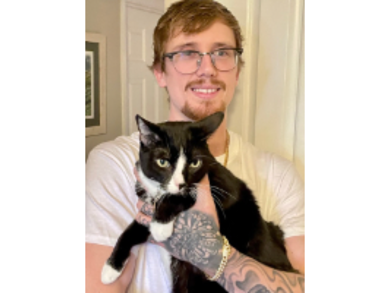 Here's an alt tag for the image: Man holding tuxedo cat.