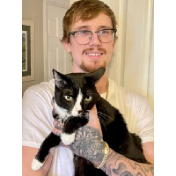 Here's an alt tag for the image: Man holding tuxedo cat.